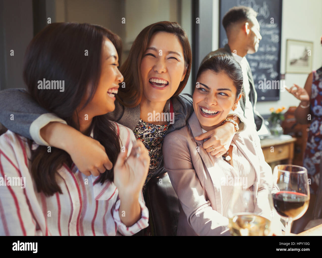 Enthusiastic, smiling women friends hugging and drinking at bar Stock Photo