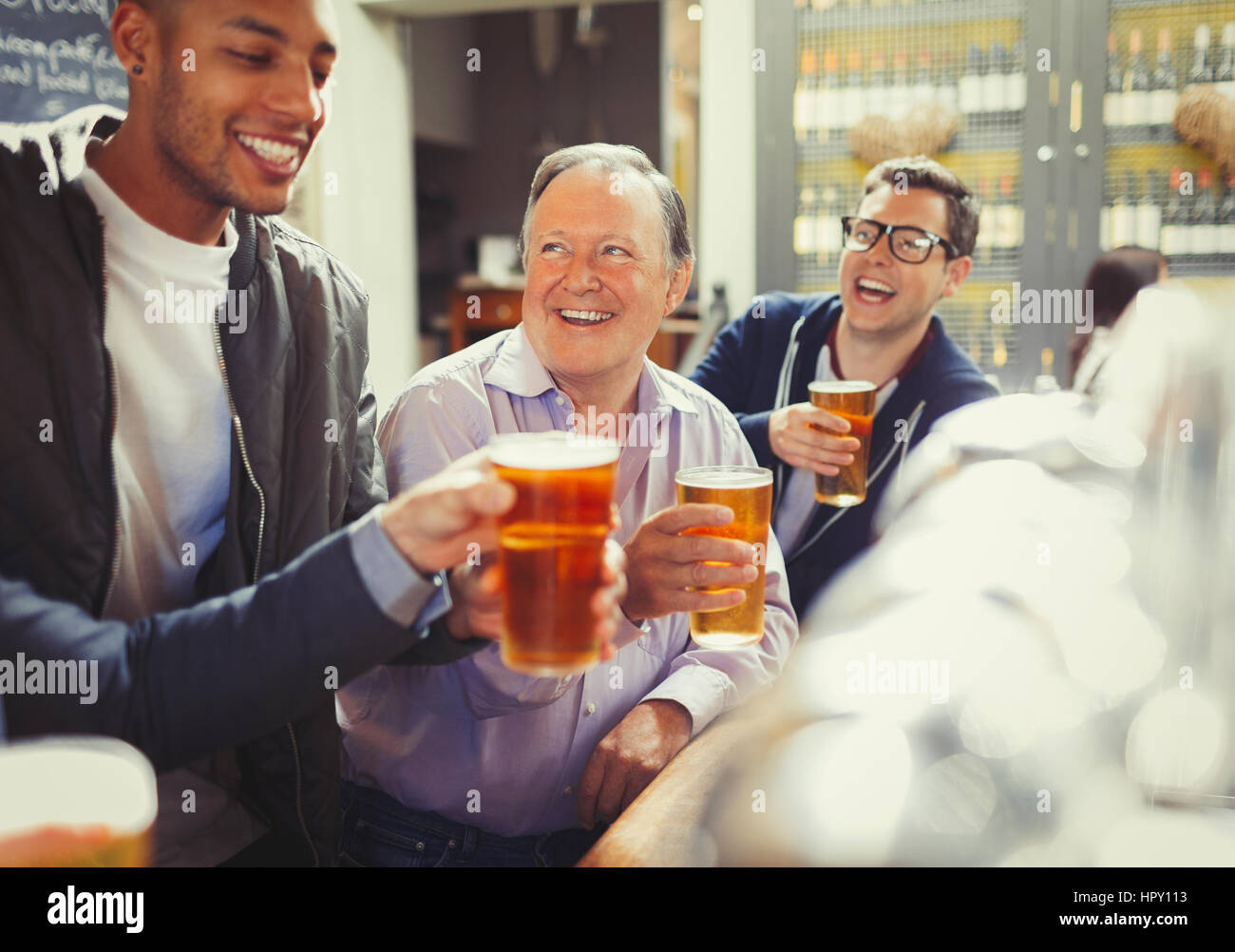 Smiling men friends toasting beer glasses at bar Stock Photo