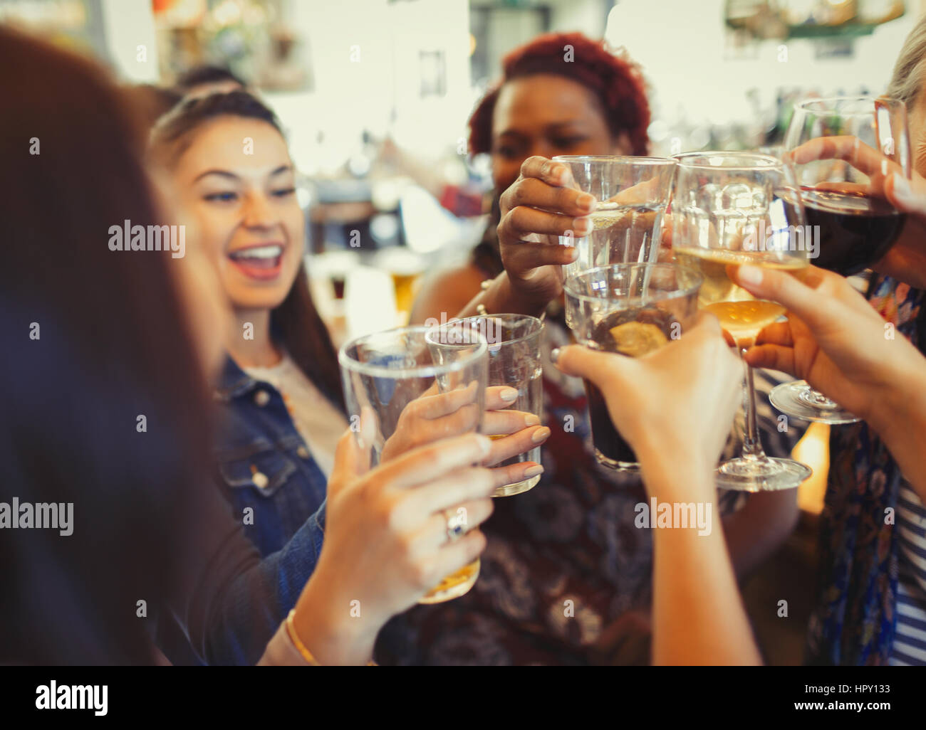 Enthusiastic women celebrating, toasting beer and wine glasses at bar Stock Photo