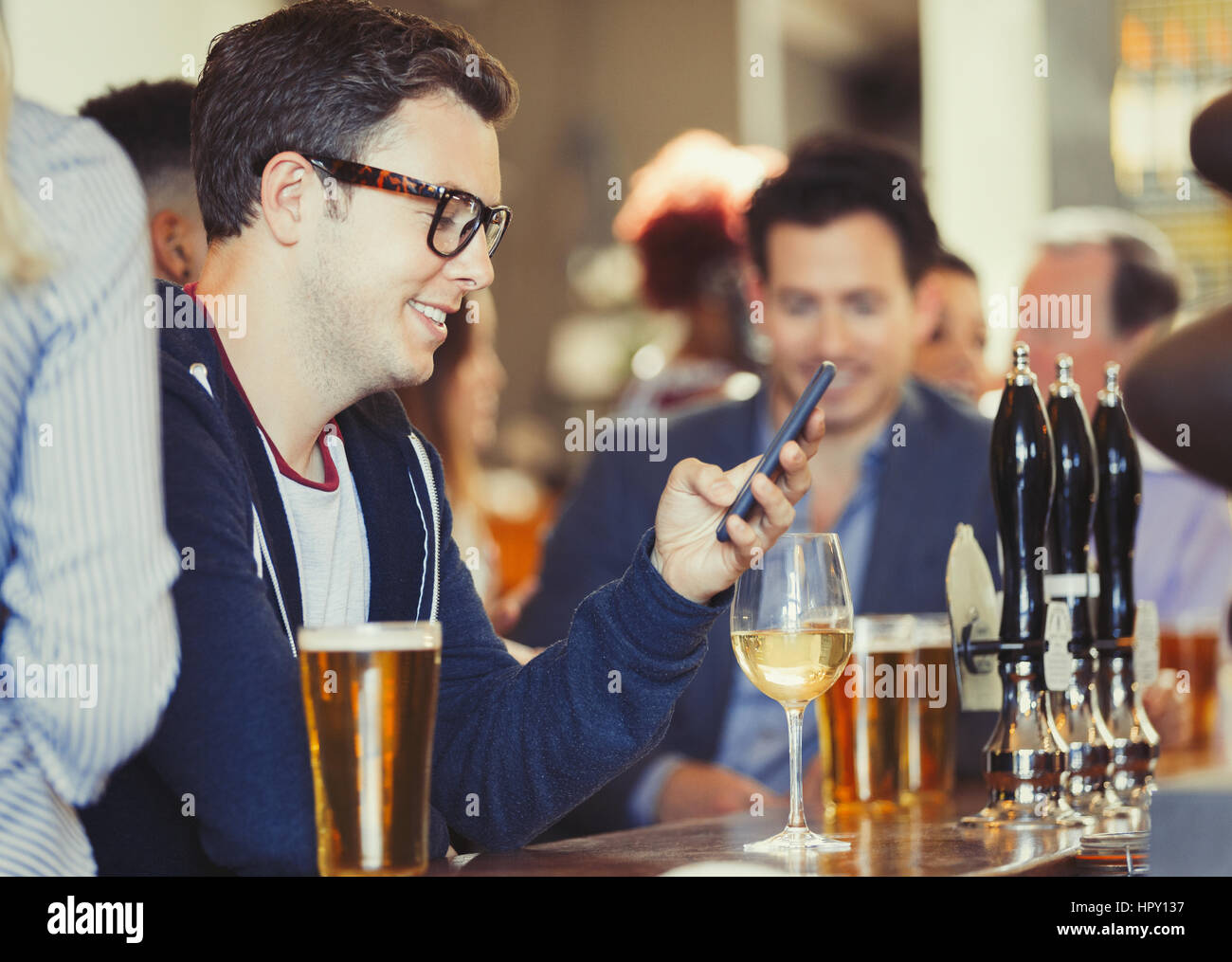 Smiling man texting with cell phone drinking wine at bar Stock Photo