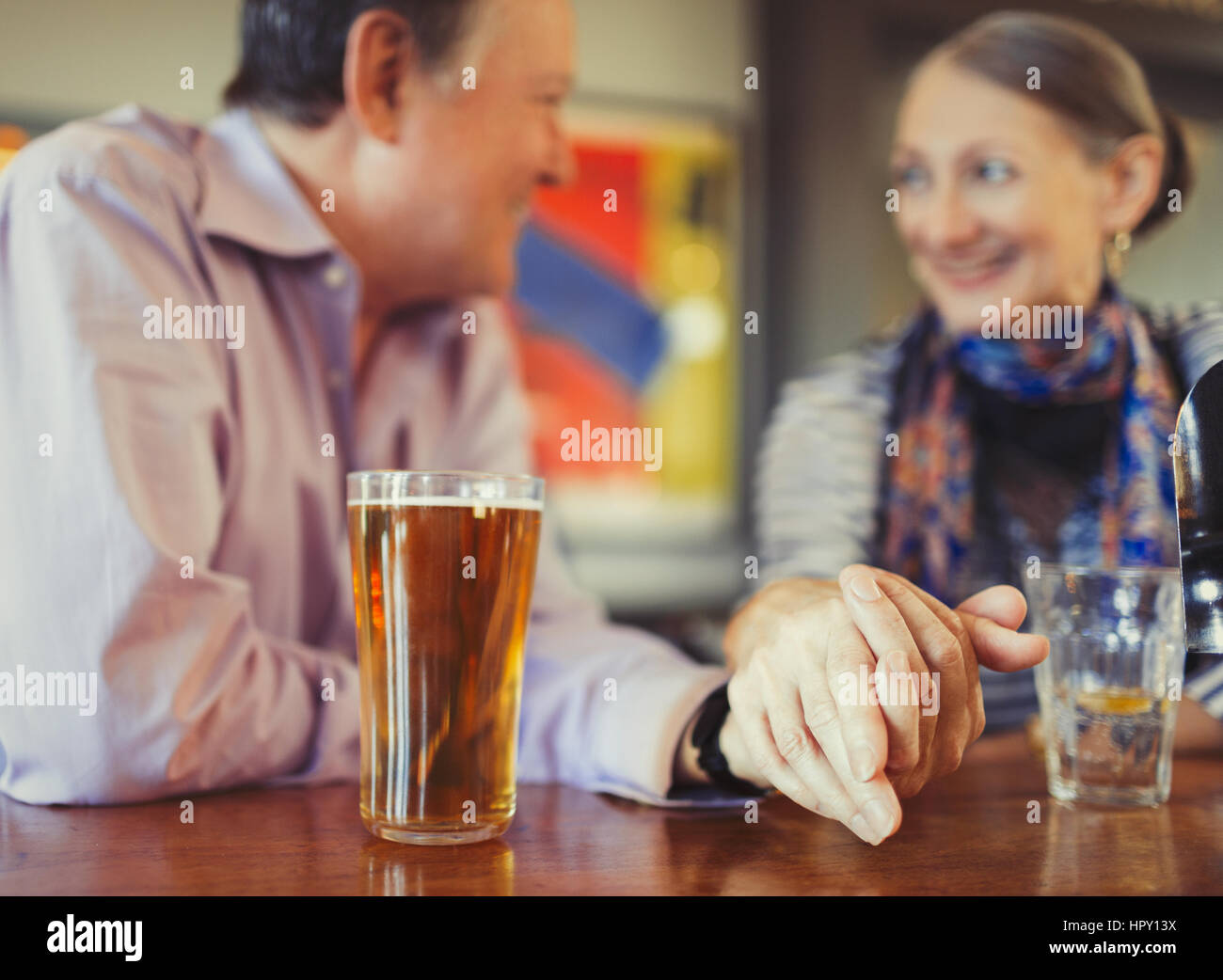 Senior couple holding hands drinking beer at bar Stock Photo
