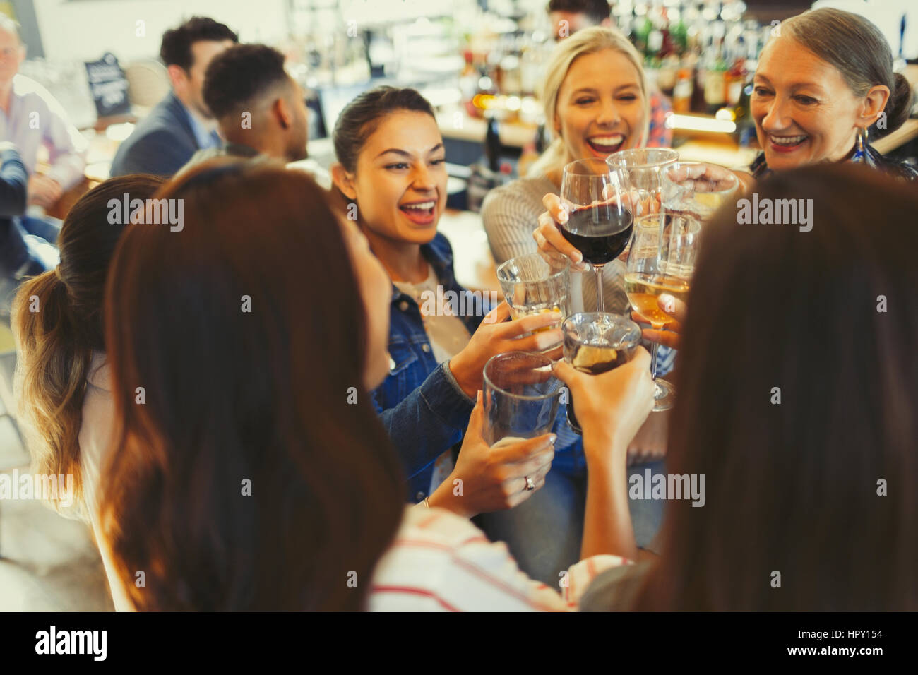 Enthusiastic women friends celebrating, toasting beer and wine glasses in bar Stock Photo