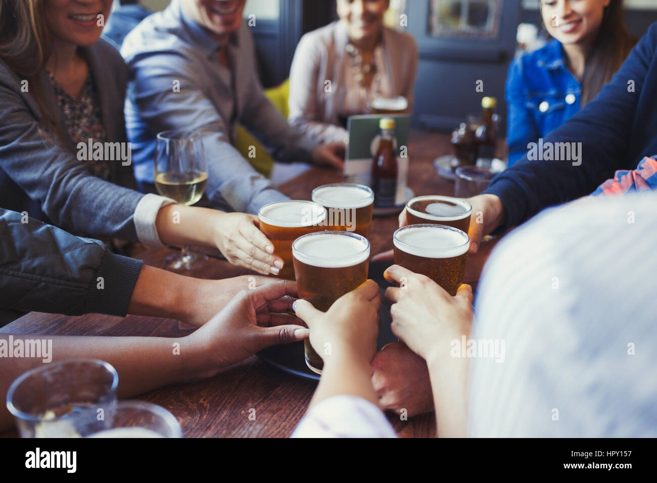 Friends reaching for beer glasses on bar table Stock Photo