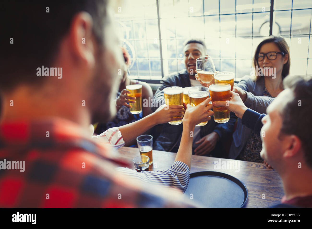 Friends celebrating, toasting beer glass at bar table Stock Photo