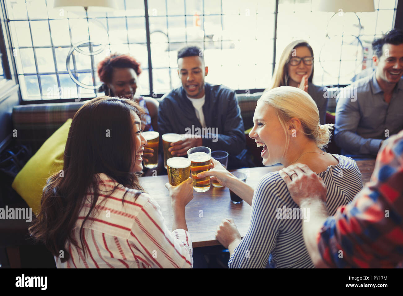 Laughing friends toasting beer glasses at table in bar Stock Photo