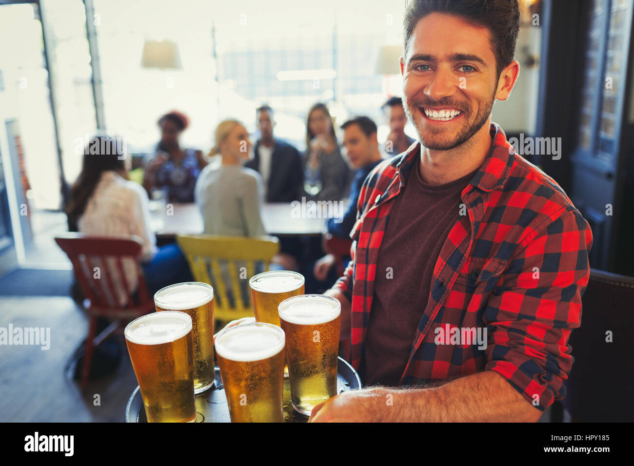 Portrait smiling bartender carrying tray of beer glasses in bar Stock Photo