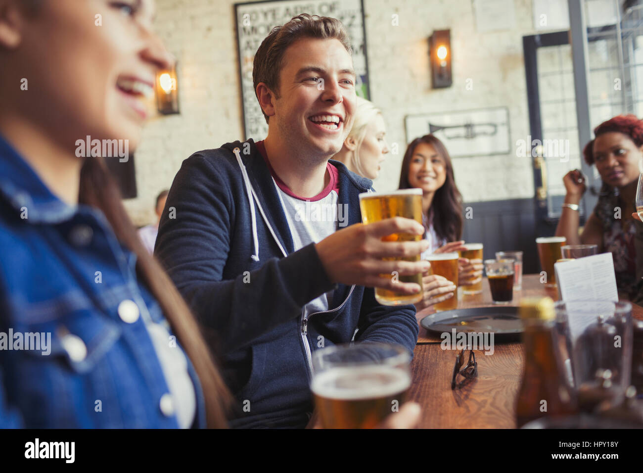 Smiling man drinking beer with friends at table in bar Stock Photo