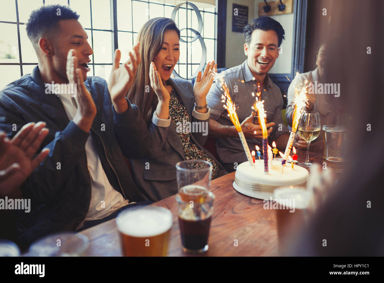 Friends cheering for woman celebrating birthday with fireworks cake at table in bar Stock Photo