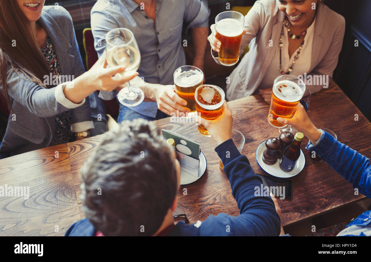 Overhead view friends celebrating, toasting beer and wine glasses at table in bar Stock Photo