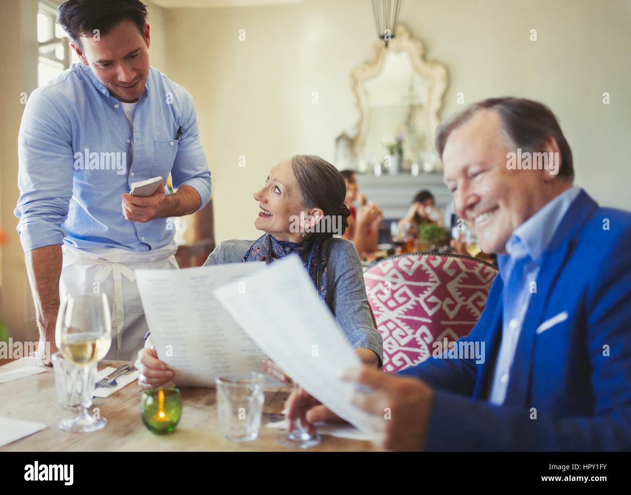 Waiter taking order from senior couple with menus at restaurant table Stock Photo