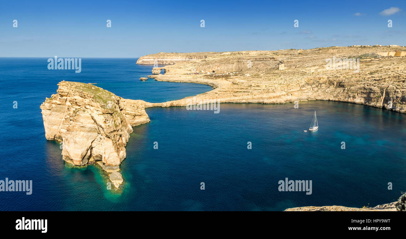 Gozo, Malta - Panoramic view of the beautiful Fungus rock with the Azure Window and sail boat at Dwejra bay on a beautiful summer day with clear blue  Stock Photo
