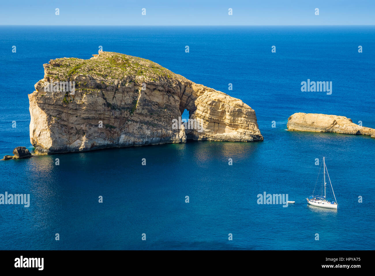 Gozo, Malta - The amazing Fungus Rock at Dwejra bay with sailboat, blue sea water and sky on a beautiful summer day Stock Photo