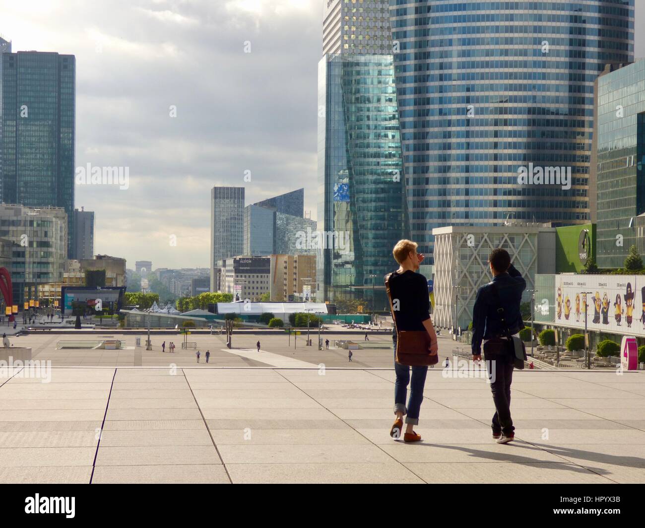 Two young men wearing messenger bags walk away from the camera on the Promenade at La Défense. Paris, France. Stock Photo
