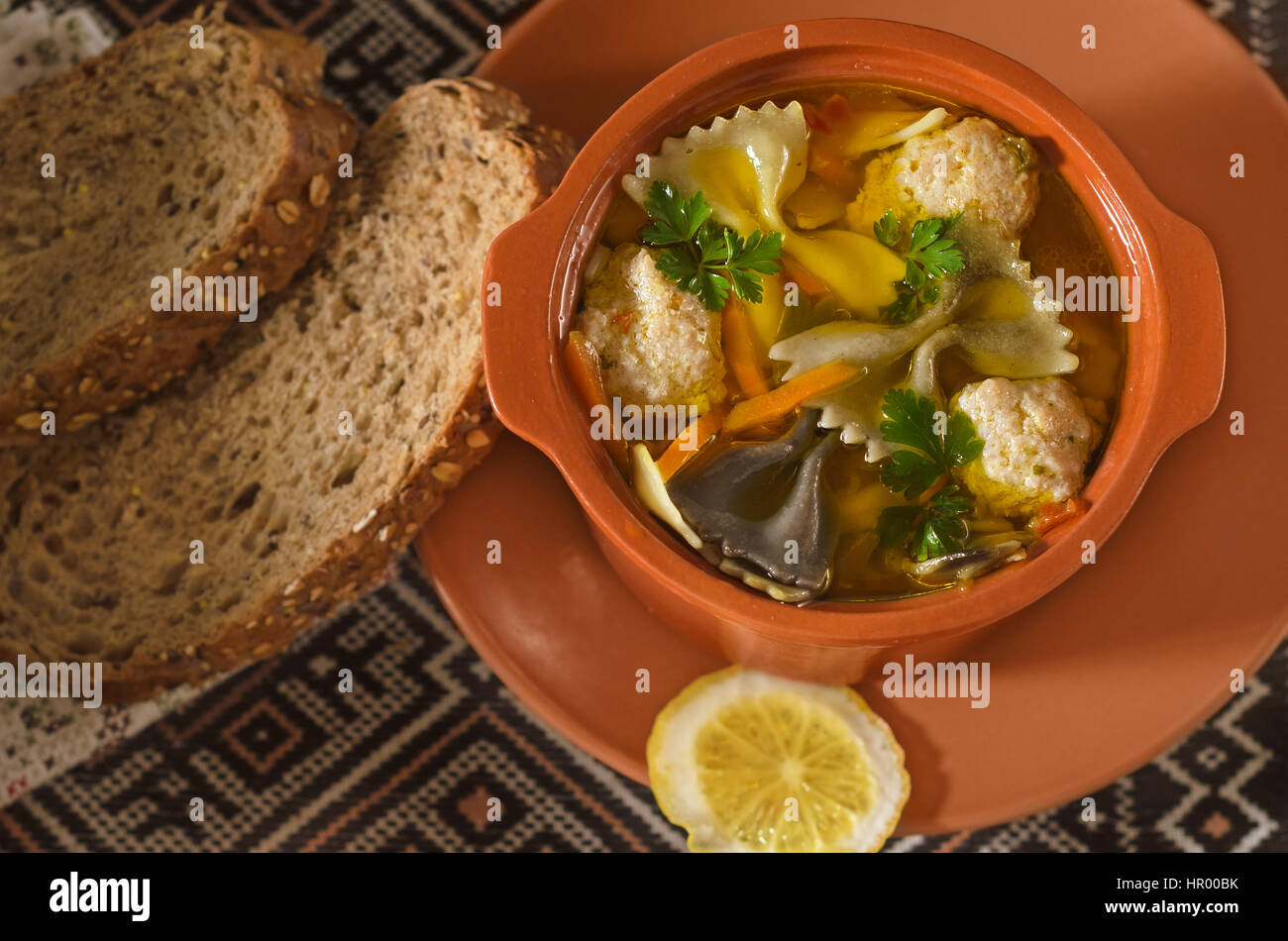 Italian soup in a ceramic pot and bread on an old embroidered towels. Low key, selective focus. Stock Photo