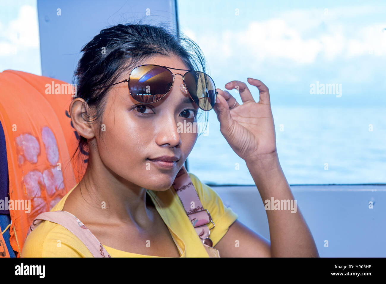 Woman with sunglasses sit on a ship beside window with view at the sea. Woman passenger traveling in a ferry at sea. Stock Photo
