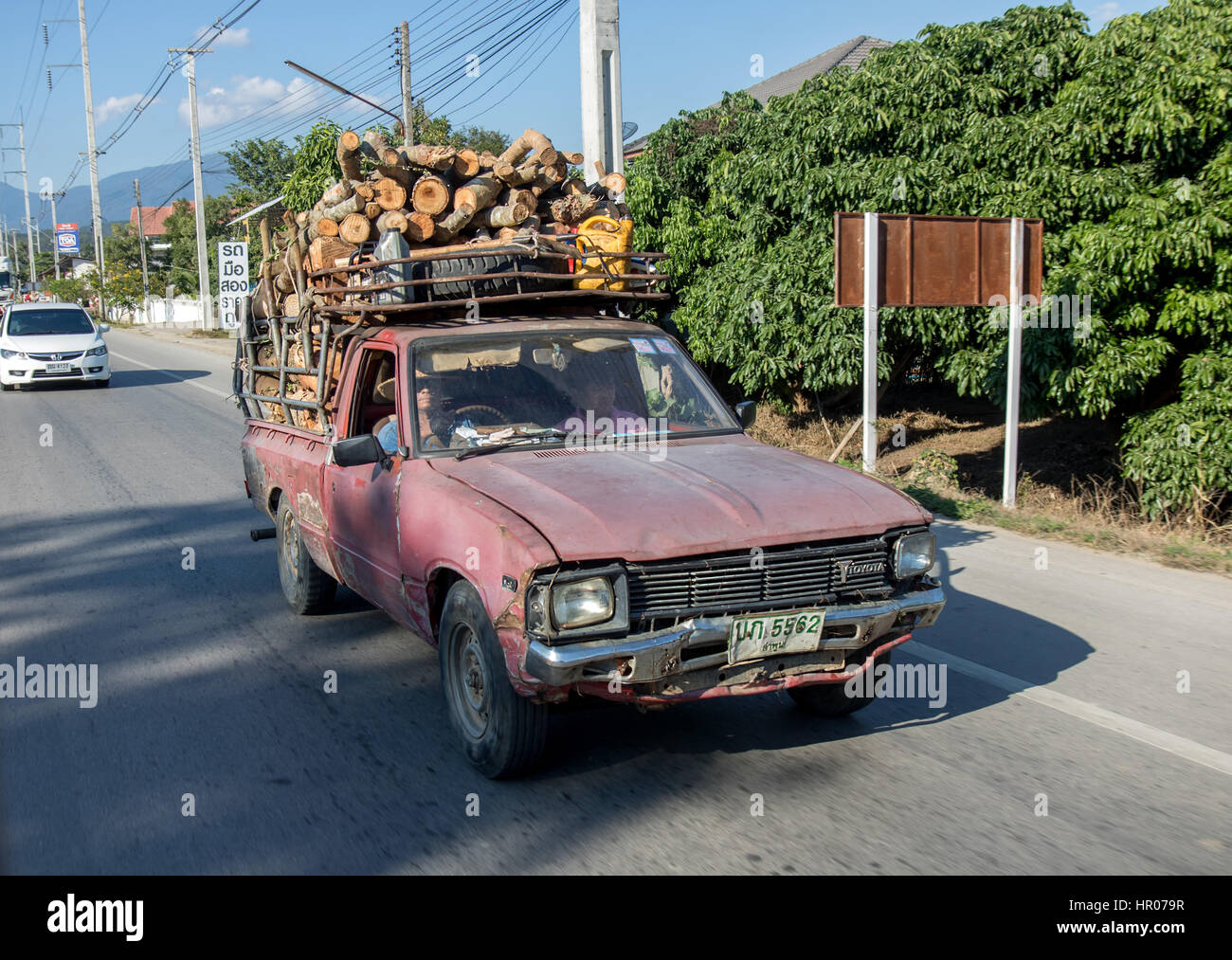 Pickup with a load of wood ride on the road at Thailand Stock Photo