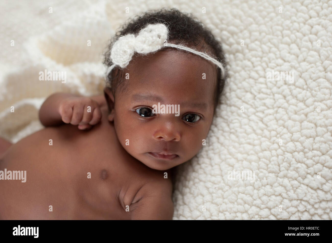 Portrait of a one month old, newborn baby girl. She is wearing a crocheted, mohair headband and lying on a soft, cream colored, faux sheepskin blanket Stock Photo