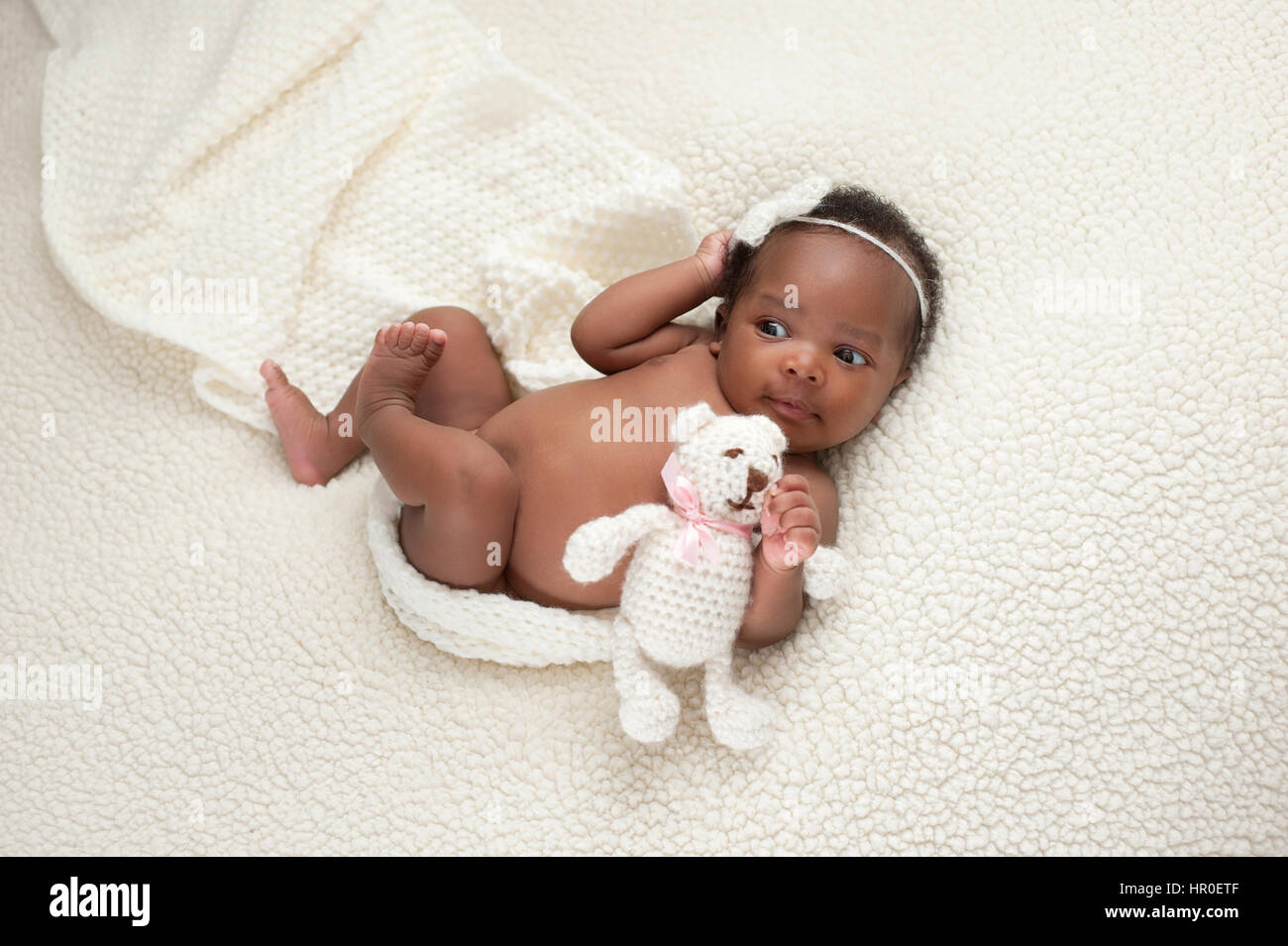 Portrait of a one month old, newborn baby girl. She is holding a stuffed bear and lying on a soft, cream colored, faux sheepskin blanket. Stock Photo
