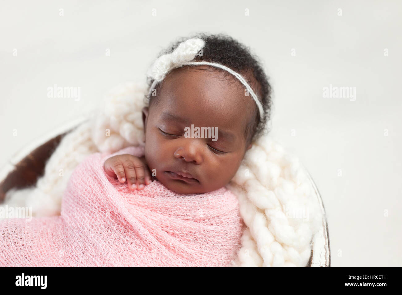 Portrait of a one month old, sleeping, newborn, baby girl. She is swaddled in pink and sleeping in a tiny bucket. Stock Photo