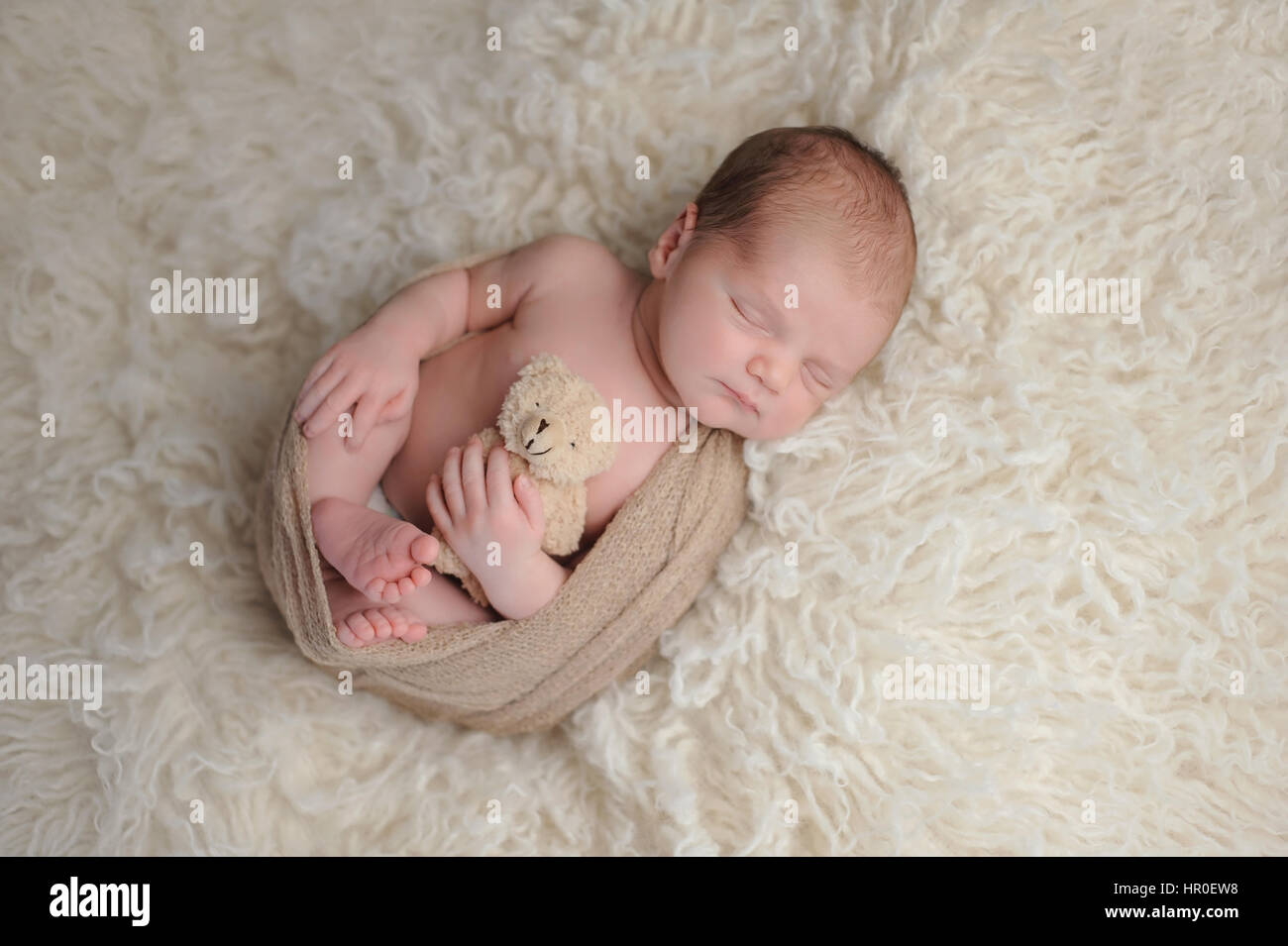 Two week old newborn baby boy swaddled in a beige wrap. He is sleeping