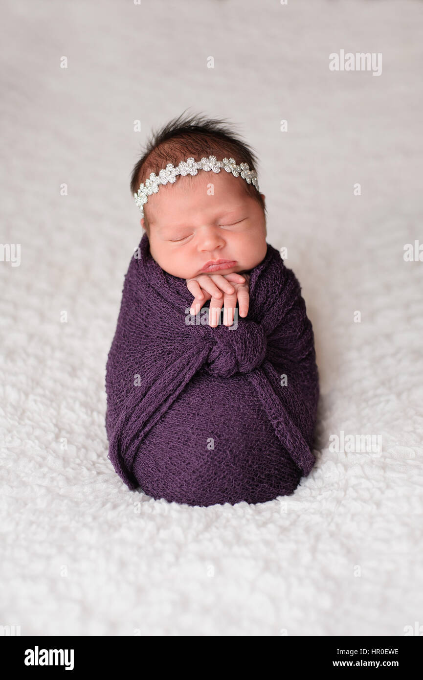 Sleeping, nine day old newborn baby girl swaddled in a purple wrap. Shot in the studio on a white blanket. Stock Photo