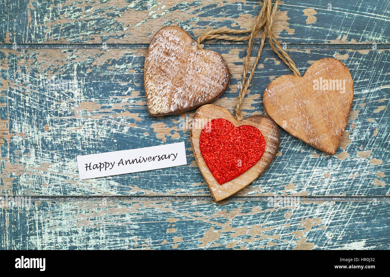 Happy Anniversary card with three wooden hearts on rustic wooden surface Stock Photo