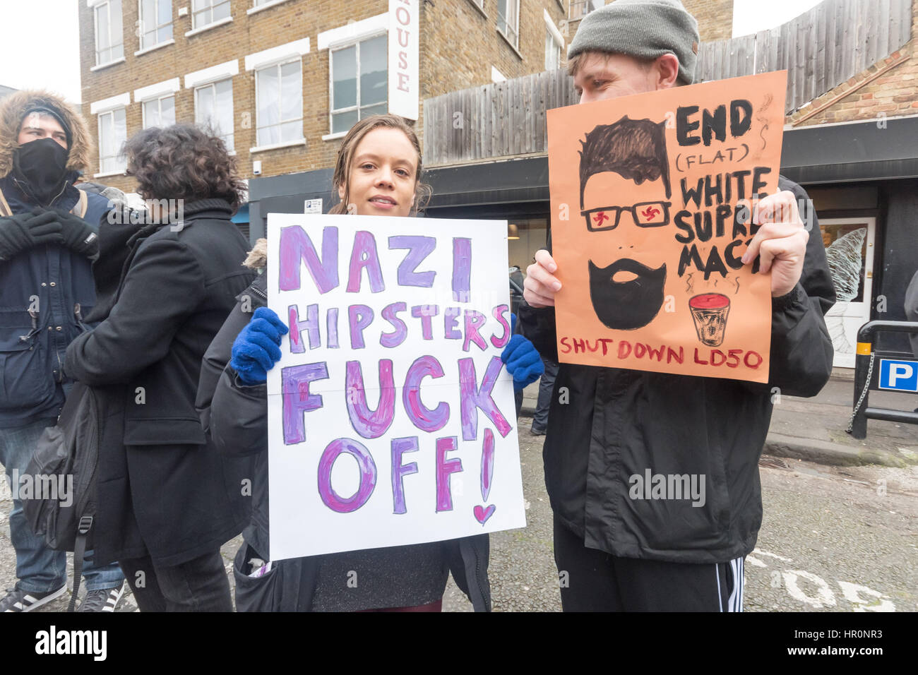 London, UK. 25th February 2017. Two of several hundred people from East London outside the LD50 gallery in Dalston hold posters against Nazi hipsters. Protesters say the gallery, named after the dose that kills half of those who take a poison, is in one of London's more diverse areas has promoted fascists, neo-Nazis, misogynists, racists and Islamophobes and 'has been responsible for one of the most extensive neo-Nazi cultural programmes to appear in London in the last decade.' The protesters want the gallery to be closed. Credit: Peter Marshall/Alamy Live News Stock Photo