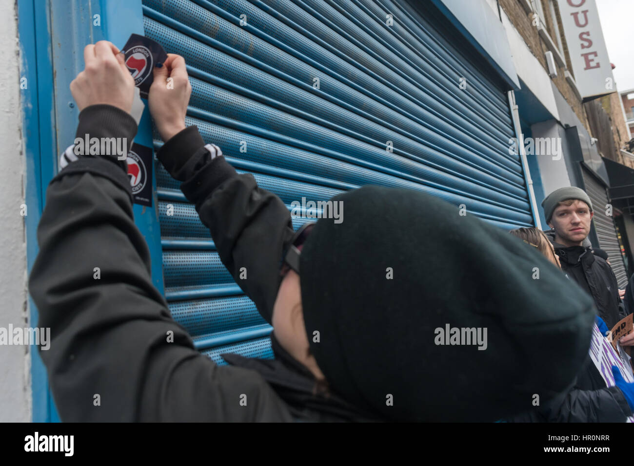 London, UK. 25th February 2017. An anti-fascist protest puts a sticker on the shopfront below the LD50 gallery in Dalston where several hundred people from East London have gathered to call for it to be shut down. They say the gallery, in one of London's more diverse areas, has promoted fascists, neo-Nazis, misogynists, racists and Islamophobes.  and, 'has been responsible for one of the most extensive neo-Nazi cultural programmes to appear in London in the last decade. Credit: Peter Marshall/Alamy Live News Stock Photo
