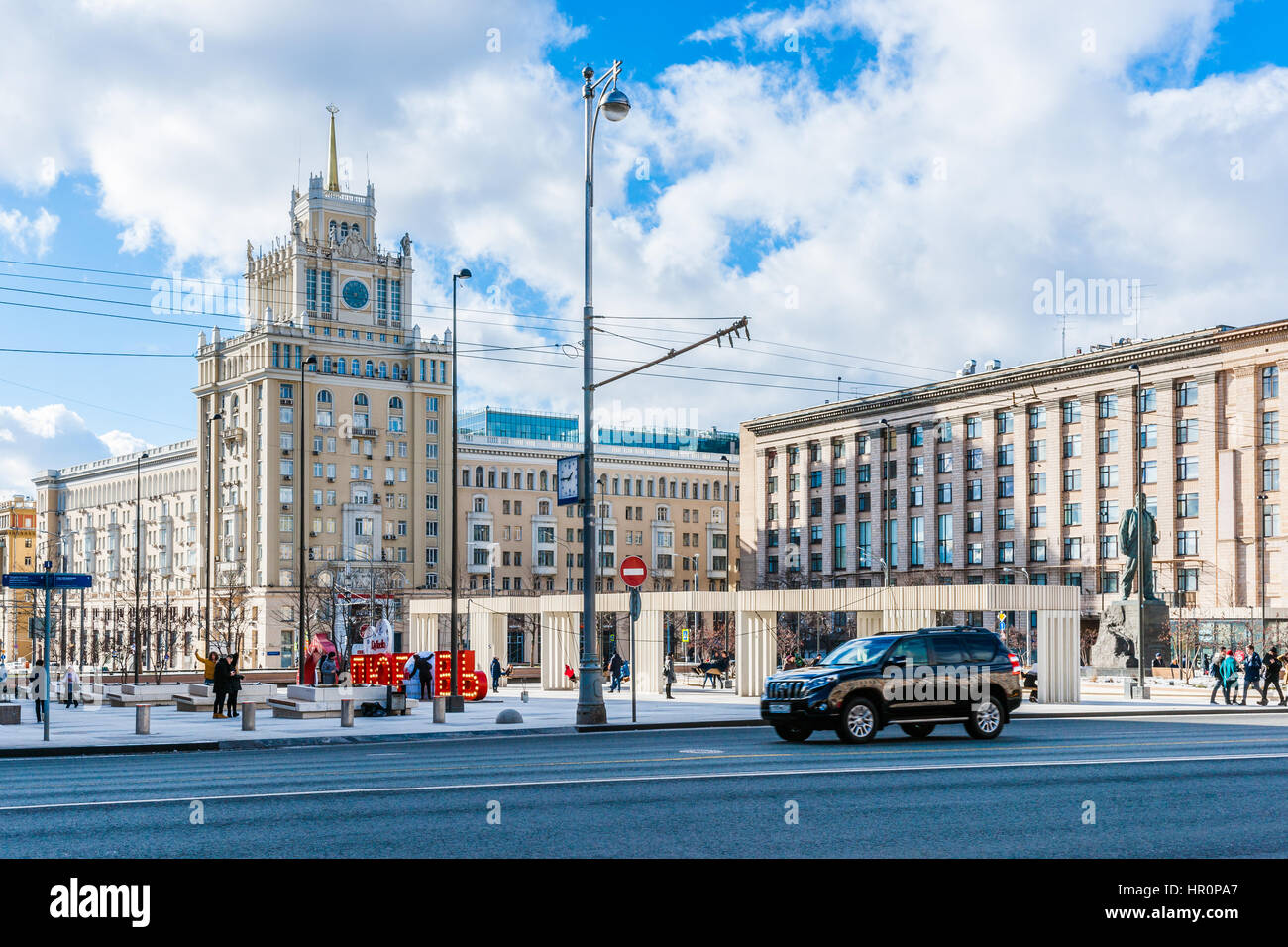 Moscow, Russia. Saturday, Feb. 25, 2017. Renovated Triumphal square, the red sign LOVE (and Raffaello candies), tall building of the Pekin (Beijing) hotel (center). This is the four star hotel, the building is of Stalin's era architecture and is listed as an architectural heritage construction. Sunny day in Moscow, but still cold temperature about -1C (30F). Sunlight flooded renovated and restored streets and squares of the big city. Mix of old and new styles of architecture and styles of life. Stock Photo
