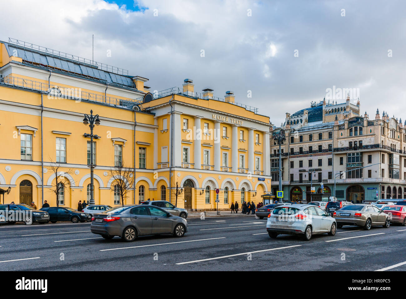 Moscow, Russia. Saturday, Feb. 25, 2017. Renovated and repaired yellow building of Maly (small as opposed to Bolshoi, grand) drama theater on Teater square of Moscow. Metropol hotel in the background. Sunlight flooded renovated and restored streets and squares of the big city. Mix of old and new styles of architecture and styles of life. Stock Photo