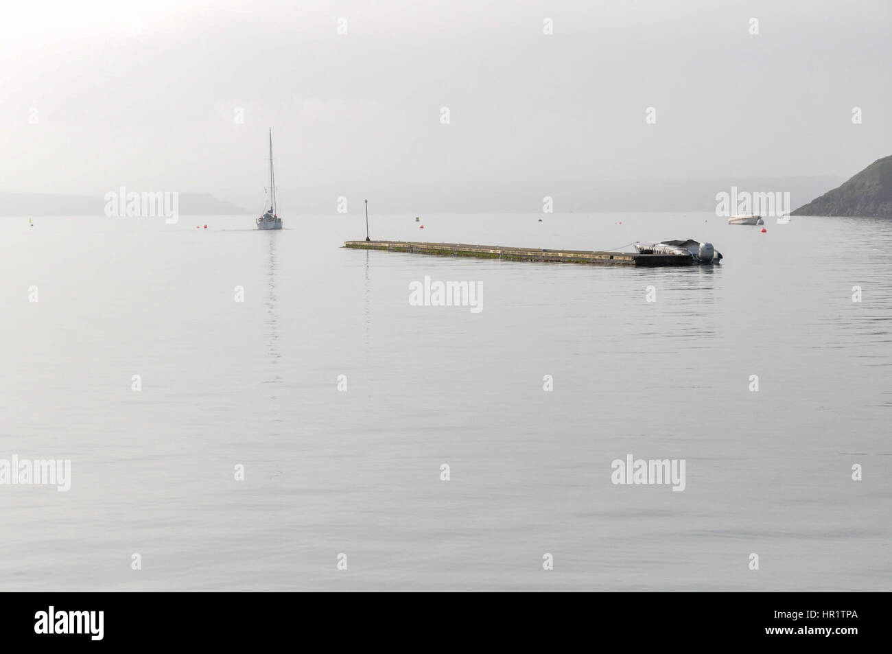 A sailing yacht making an early start as it motors away from the outer pontoon at Dale in the mist of a calm summers morning Stock Photo