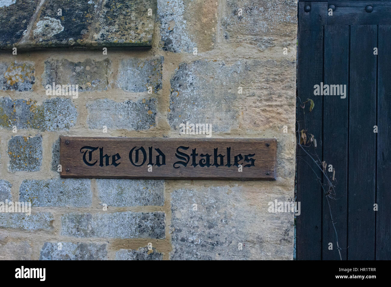 A traditional wooden sign for The Old Stables on a Cotswold village wall Stock Photo