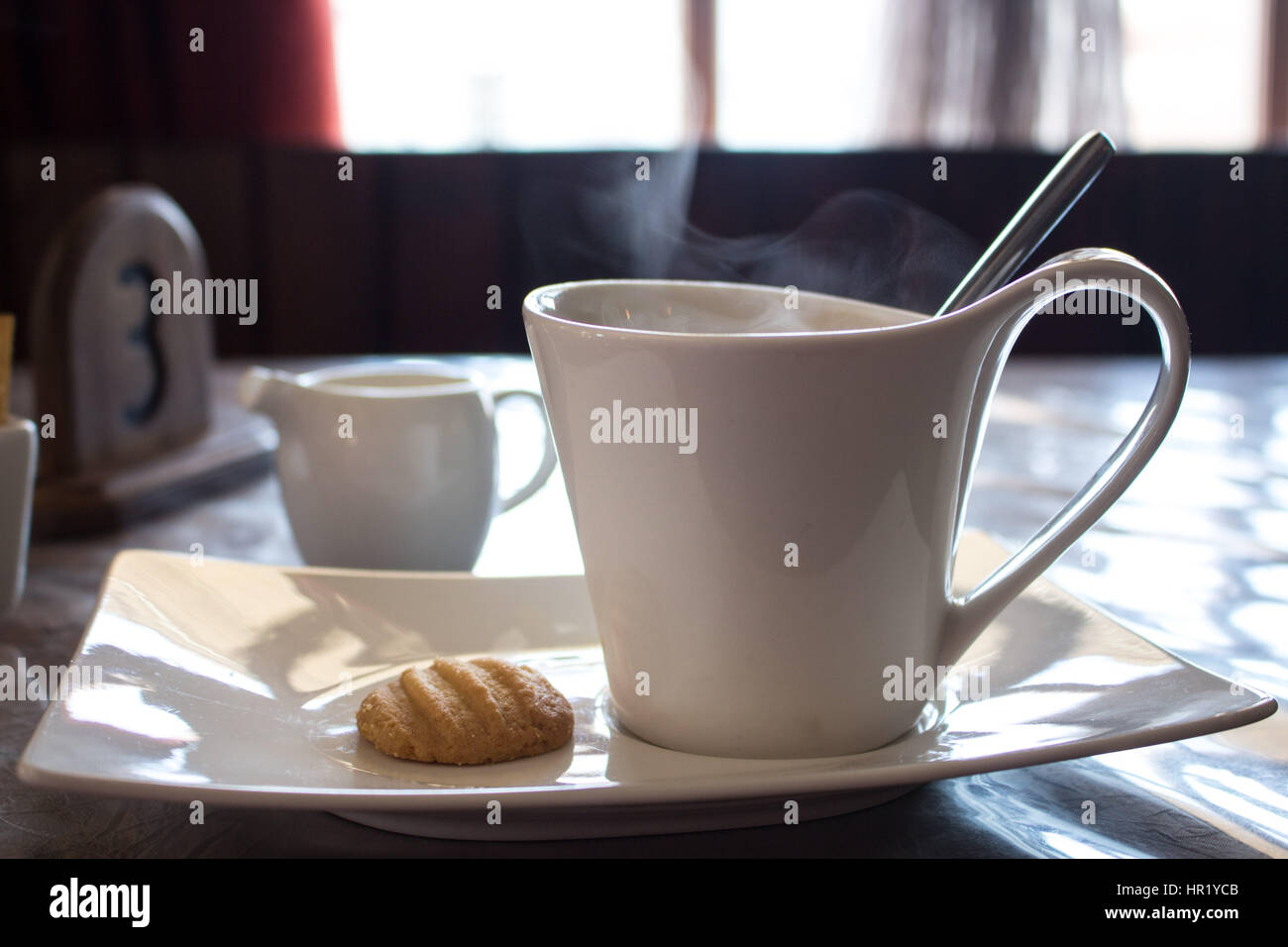 White cup of coffee on a plate with a cookie on a table, Diaz Coffee Shop, Luderitz. Namibia. Stock Photo
