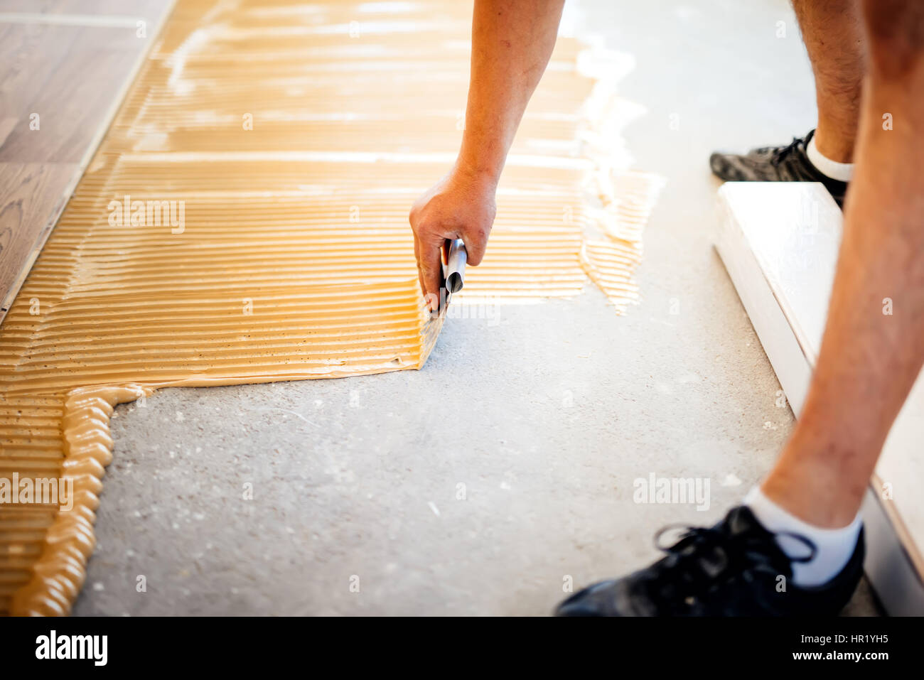 industrial worker adding glue on cement floor, preparing surface for wood parquet Stock Photo