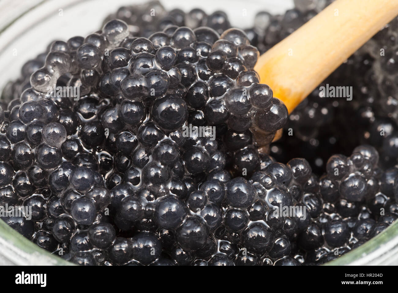 black dyed salty caviare of halibut fish with wood spoon close up in glass jar Stock Photo