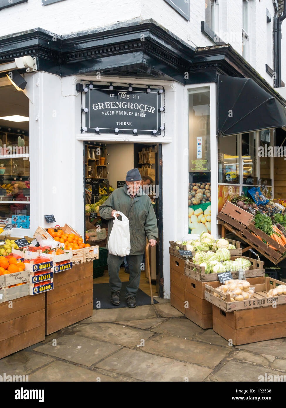An old man exiting a greengrocers shop carrying a bag of vegetables in Thirsk North Yorkshire Stock Photo