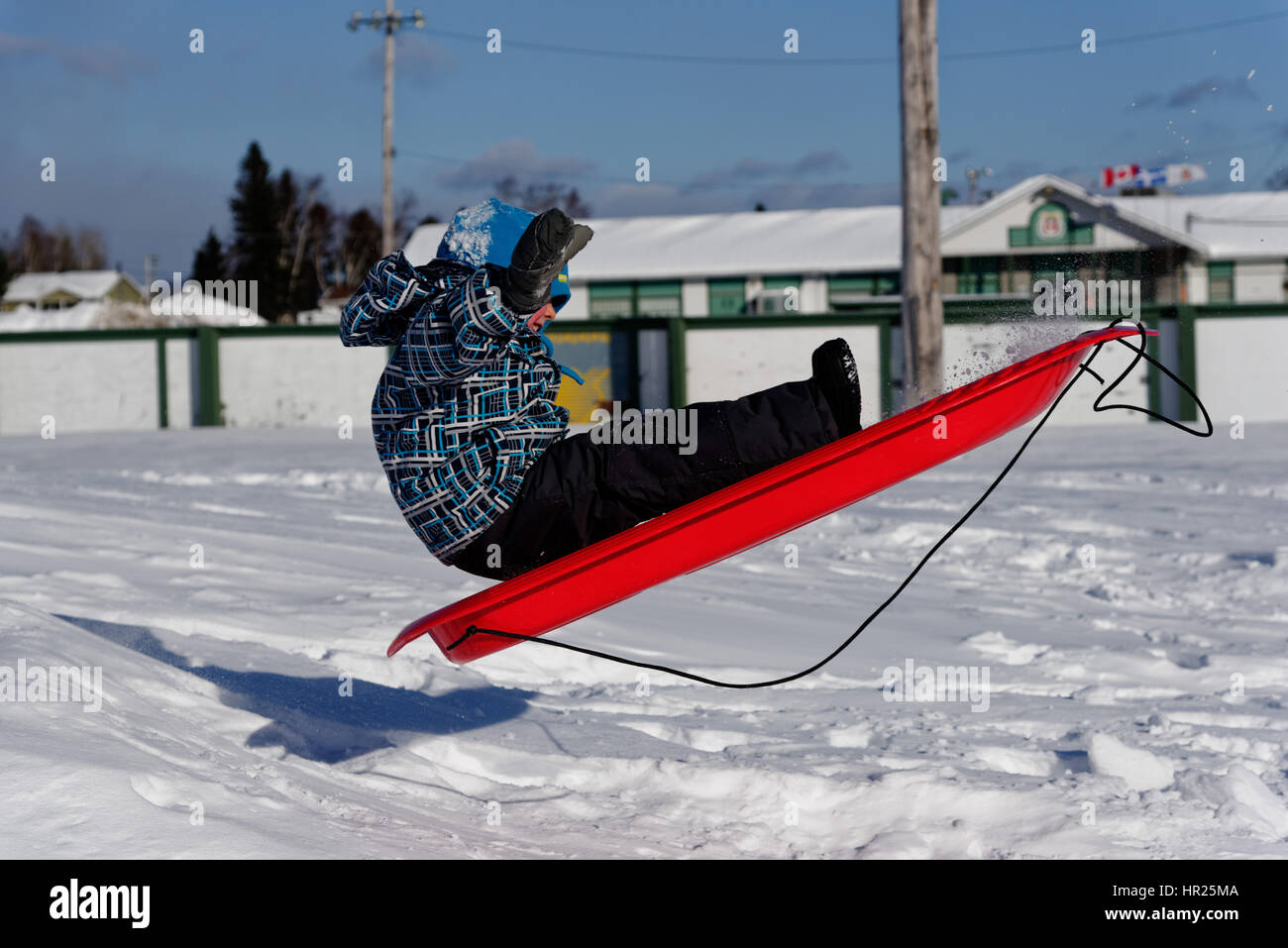 A young Boy (4 yrs old) jumping into the air on a sledge in Quebec winter Stock Photo