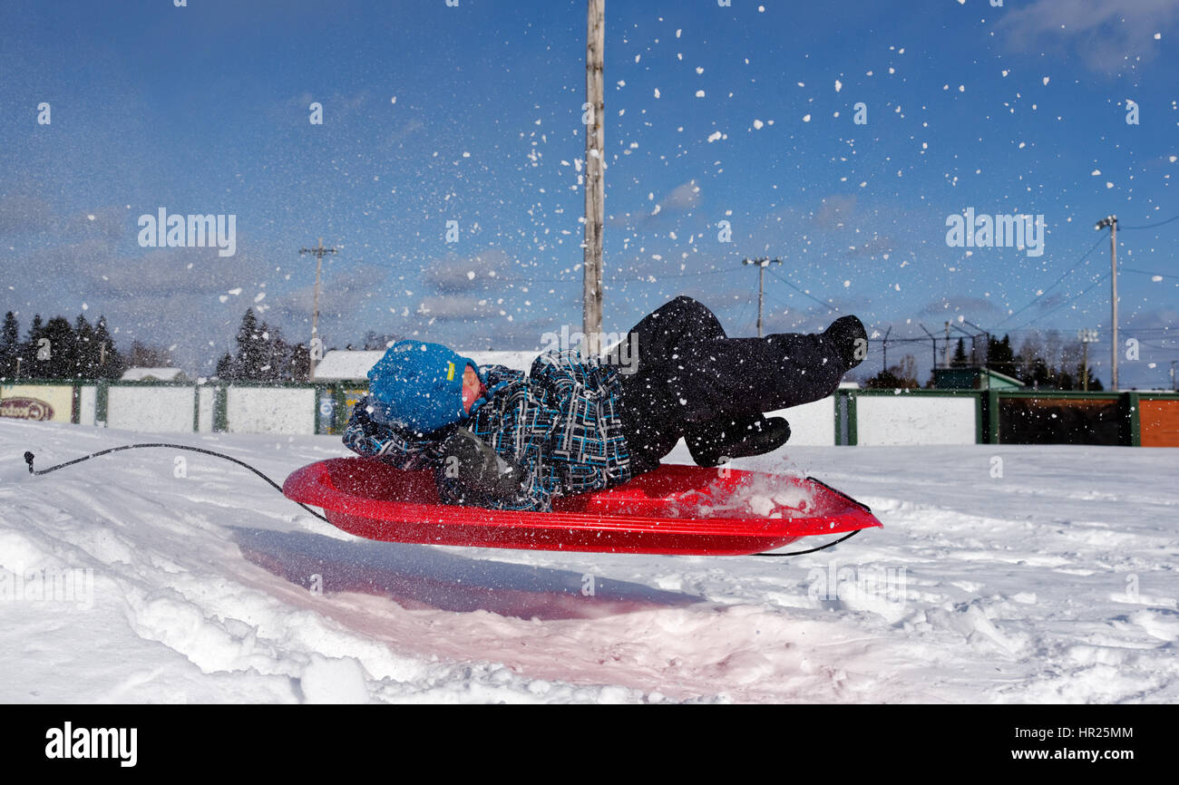 A young Boy (4 yrs old) jumping into the air on a sledge in Quebec winter Stock Photo