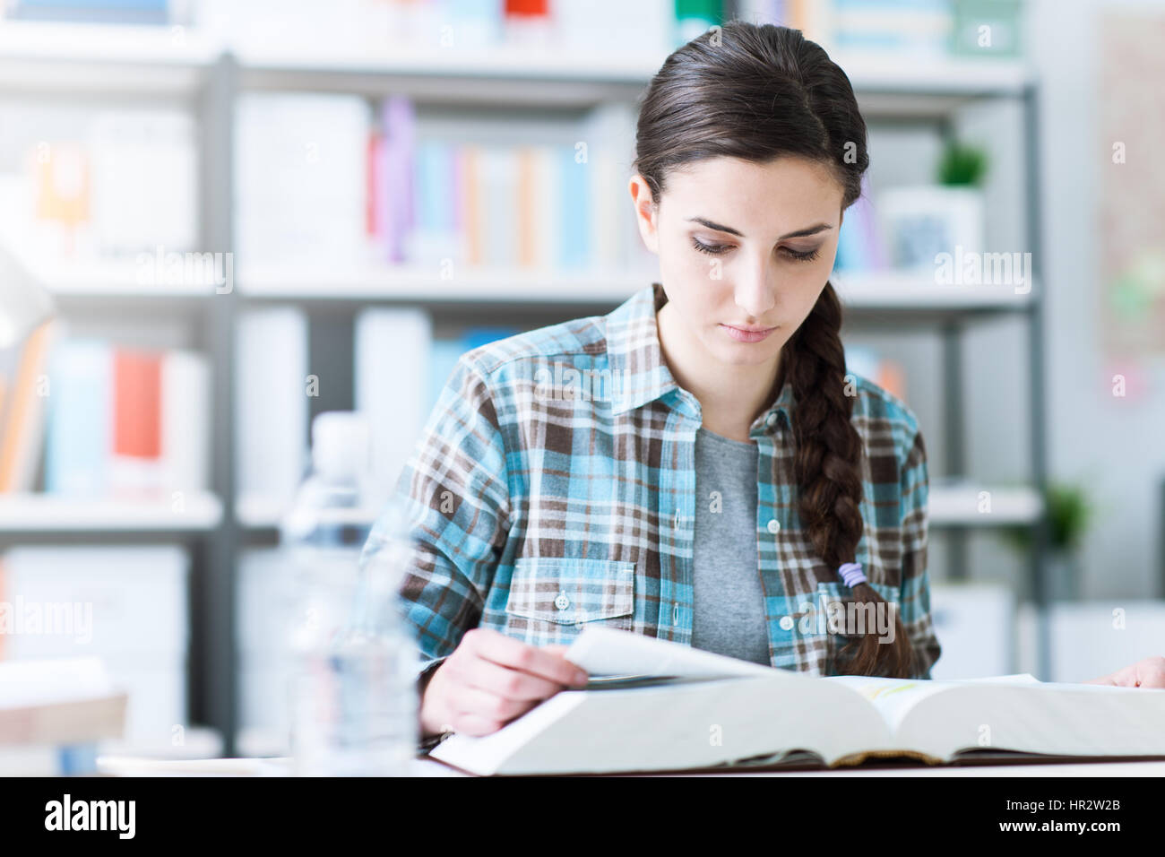 Smart College Student In The Library Sitting At Desk And Reading A