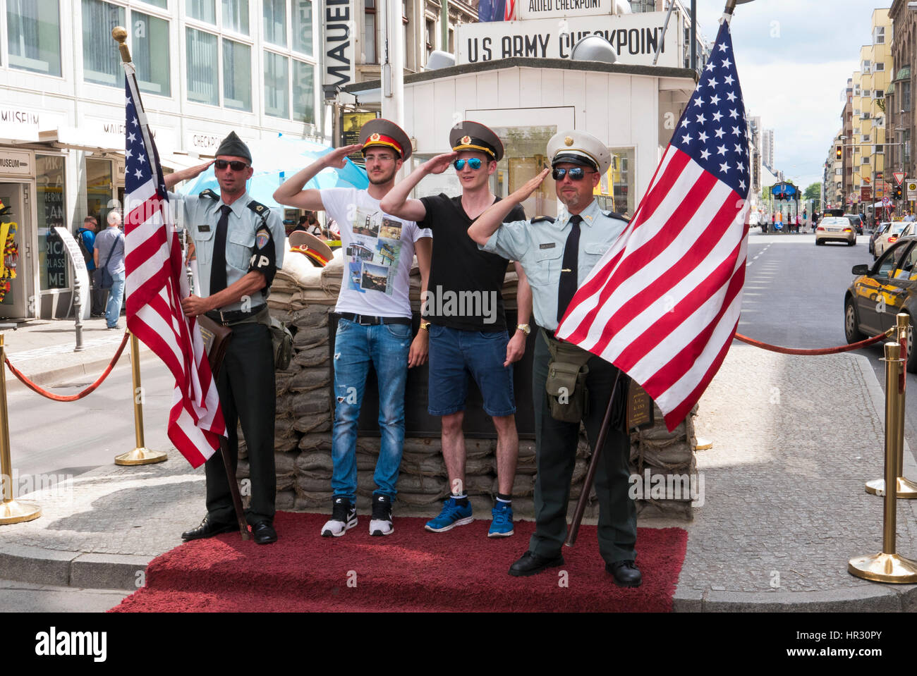 Two uniformed men holding American flags and two male tourists having photographs taken at Check Point Charlie, Berlin, Germany Stock Photo