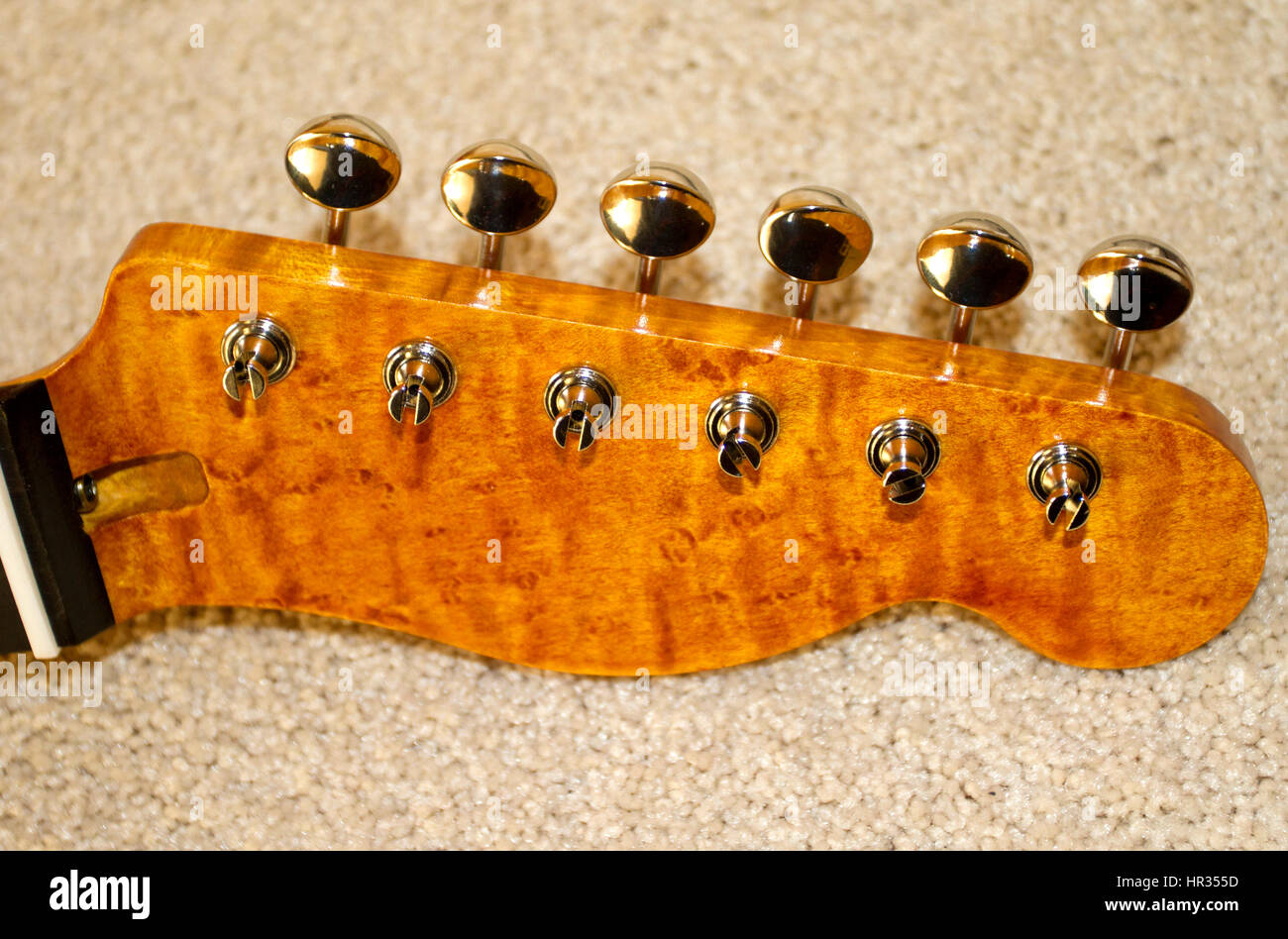 Electric guitar headstock front view, Fender design made from birds-eye maple wood, sanded, stained, lacquered and machine heads fitted Stock Photo