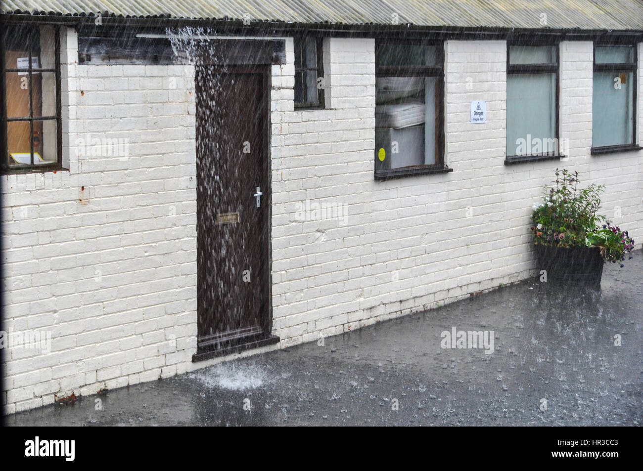 Torrential rain running over the gutters of a single storey building Stock Photo