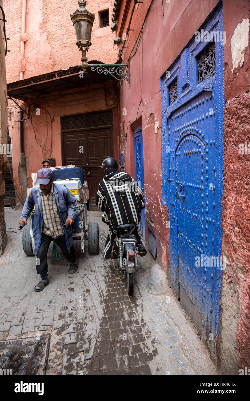 Marrakesh, Morocco.  Porter and Motor Bike Pass in Narrow Street in the Medina. Stock Photo