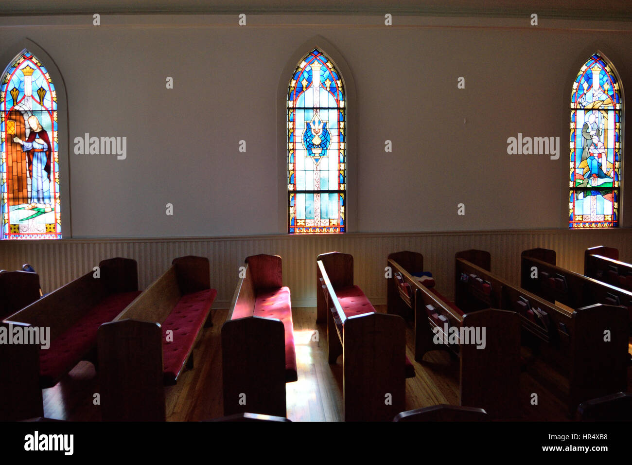 Sun shining through a stained glass window onto a pew of a small town Methodist church Stock Photo