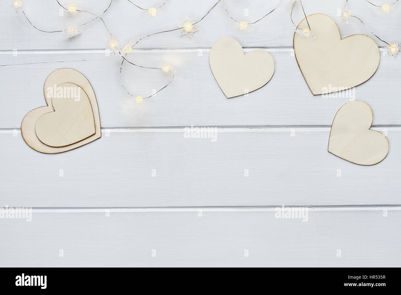 Overhead view of wooden love Valentine's hearts with lite fairy lights over a wooden background with copy space available. Stock Photo