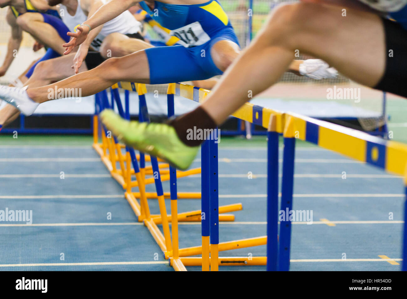 sportsmen running hurdles sprint race in indoor track and field