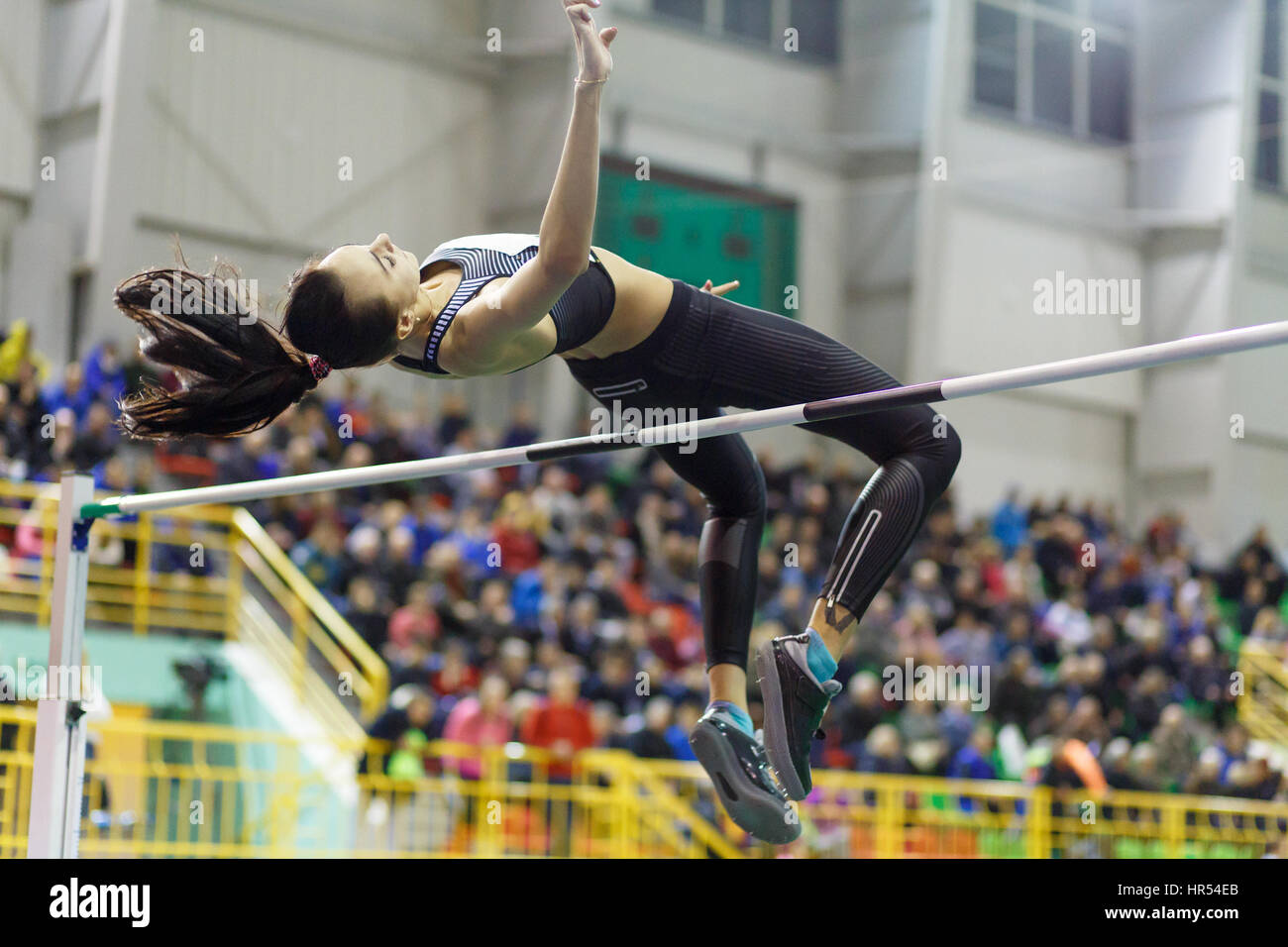 Young professional sportswoman jumping over bar in high jump