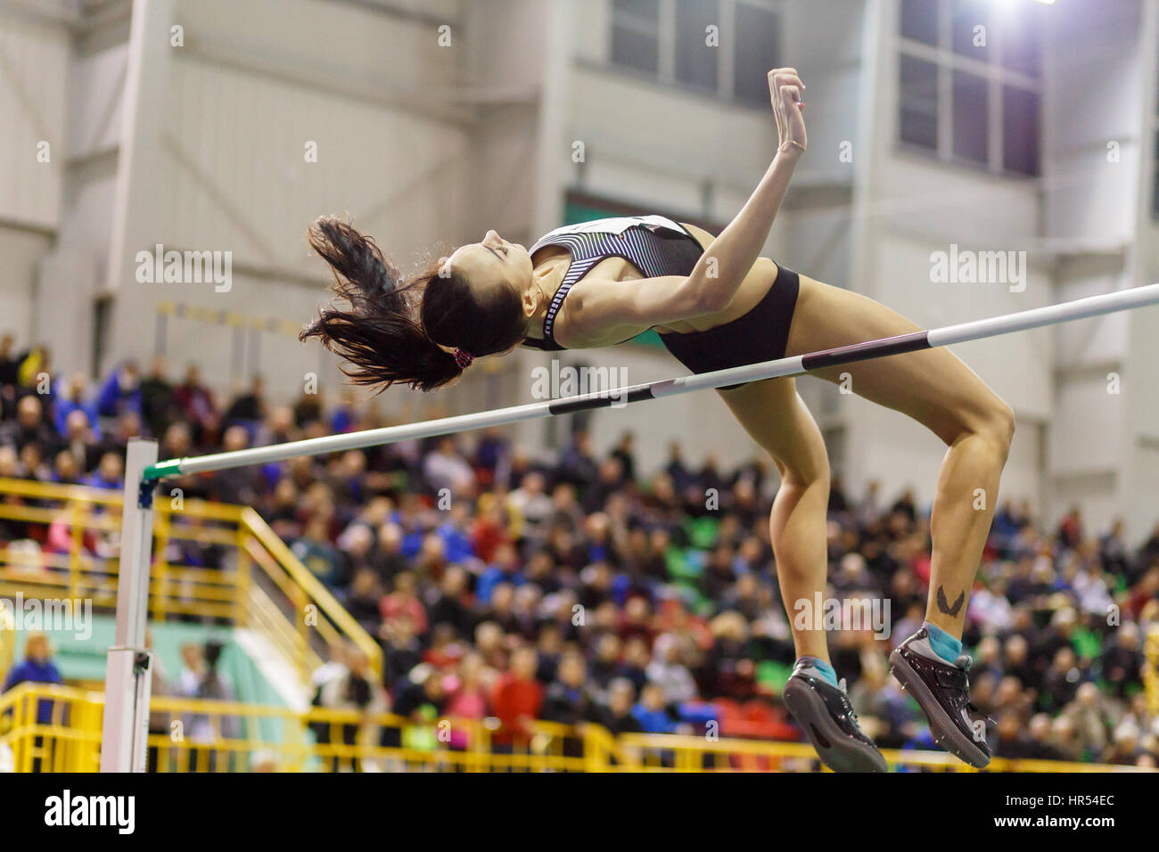 Young professional sportswoman jumping over bar in high jump