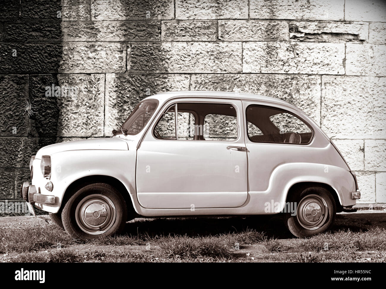 White old-timer super-mini car parked on grass against old wall in Pula, Croatia. Stock Photo