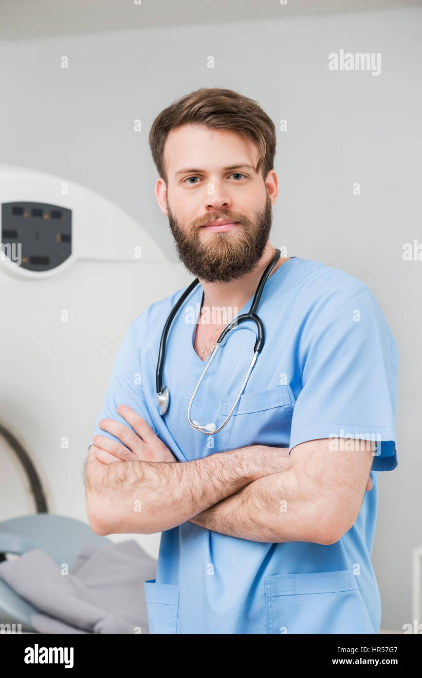 Portrait of young male doctor standing arms crossed in examination room